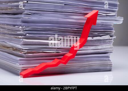 Red Increasing Growth Arrow In Front Of Stacked Document On Reflecting Table Stock Photo