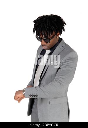 A close up image of an African American man standing in a light gray suit and black shirt looking at his watch, isolated for white background Stock Photo