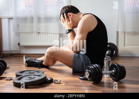 Side View Of Young Man Suffering Sitting On Hardwood Floor In Gym Stock Photo