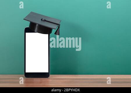 Close-up Of Graduation Hat On Blank Display Mobile Phone In Front Of Green Chalk Board Stock Photo