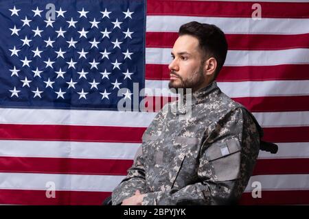 Side View Of Veteran Sitting In Wheelchair In Front Of An American Flag Stock Photo