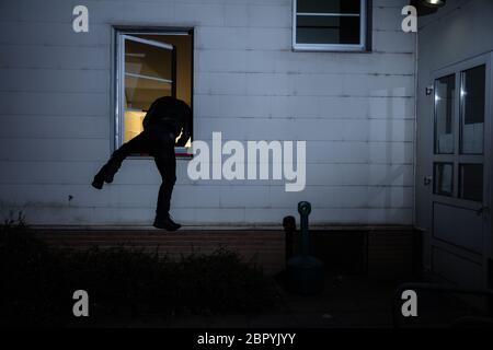 Rear View Of A Burglar Entering In A House Through A Window Stock Photo