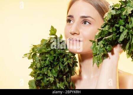 Close up of beautiful young woman with green leaves on white background. Concept of cosmetics, makeup, natural and eco treatment, skin care. Shiny and healthy skin, fashion, healthcare. Stock Photo