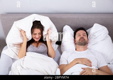 An Elevated View Of Young Woman Covering Her Ears With Pillow While Man Snoring Stock Photo