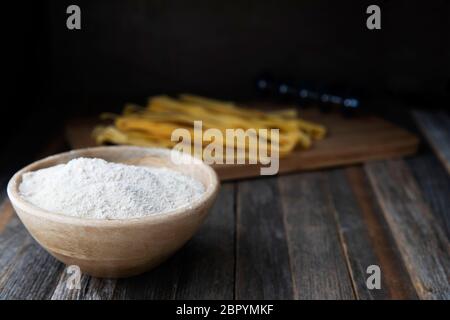 Bowl of whole wheat flour on a rustic wooden table with pappardelle pasta in the background. Stock Photo