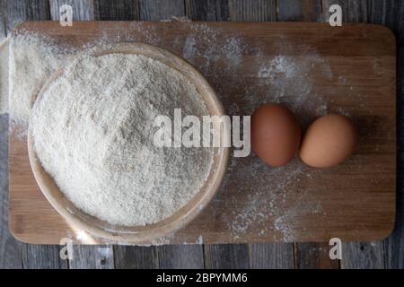 Bowl of whole wheat flour and two eggs on a cutting board. Stock Photo