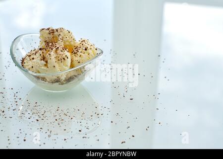 a glass bowl with vanilla ice cream sprinkled with chocolate chips, standing on a bright table in the kitchen. the bowl, window and sky are reflected Stock Photo