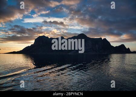 Some of the Lofoten islands above the Arctic Circle in northern Norway, seen in silhouette in late afternoon sunlight with sea in foreground Stock Photo