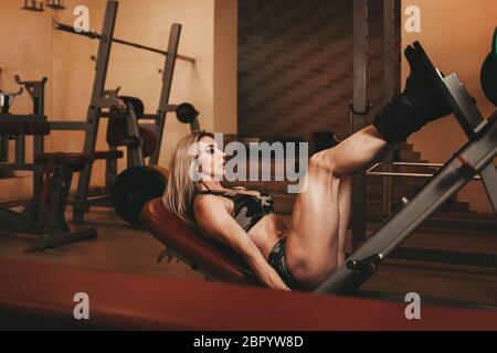 Sporty lady in gym doing leg exercises. Muscular bodybuilder works out in the gym Stock Photo