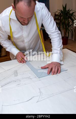 Male clothe designer drawing seamless pattern on sheets of paper with patterns for clothes. Thread Sewing Hobby, Handmade and Craft items. Tailor work Stock Photo