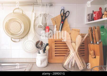 kitchen corner with various cooking utensils including a colander, knives and wooden utensils in a glass container Stock Photo