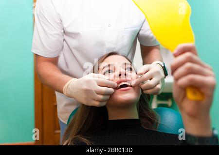 Patient woman with a beautiful smile sits in a dental chair and looks in the mirror at the result Stock Photo