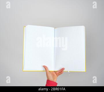female hand holds open yellow notepad into a cell on gray background, copy space Stock Photo