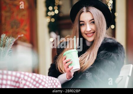 Beautiful girl in a hat sits at a cafe table with a cup of coffee in her hands Stock Photo
