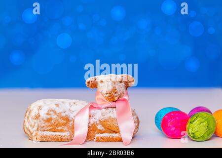 Easter decorations isolated. Macro with focus on a traditional easter lamb cake and some colorful eggs on a bright table against abstract blue backgro Stock Photo