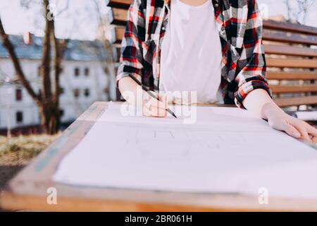 Girl draws on a board for artists directly on the city street. Pretty woman is engaged her favorite hobby at her leisure Stock Photo
