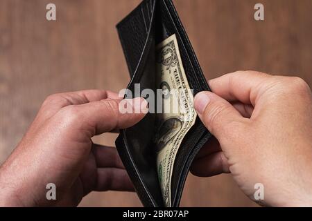 Black leather wallet with one dollar in the hands of a man. Bankruptcy and Poverty Concept Stock Photo