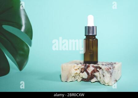 A glass dropper bottle on natural handmade soup on the green or mint background and litlle part of leaf of green monstera. Nature Skin concept. Organi Stock Photo