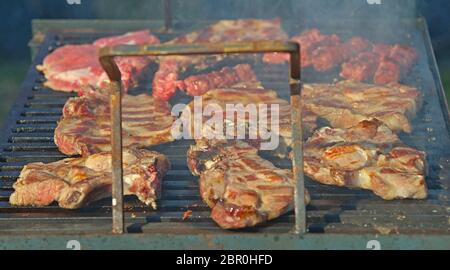 Pork chops roasting on barbeque grill with smoke around Stock Photo