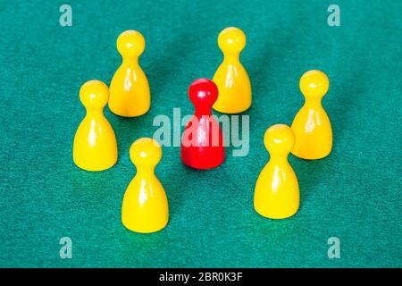 concept scene - one red pawn surrounded by yellow pawns on green baize table Stock Photo