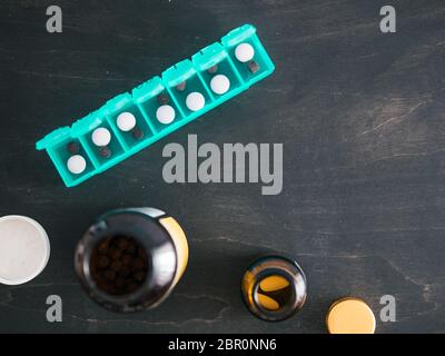 Top view of seven day pill box with pills. Green pill-box with pills visible. Open pill box and jars on dark wooden table. Copy space. Top view or fla Stock Photo