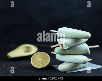Homemade raw vegan avocado lime popsicle. Sugar-free, non-dairy green ice cream on black textured background. Copy space. Ideas and recipes for health Stock Photo