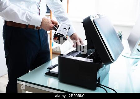 Mid-section Of Businessman Fixing Cartridge In Printer At Workplace Stock Photo