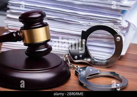 Close-up Of Gavel And Handcuffs Near Stacked Paper On Wooden Table Stock Photo