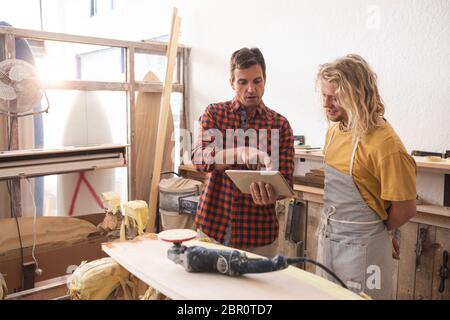 Two Caucasian male surfboard makers discussing the project and using a tablet computer Stock Photo
