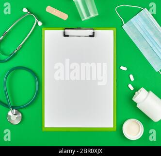 paper holder with empty white sheets, medical stethoscope, pills and textile bandage on a green background, top view, space for writing a prescription Stock Photo