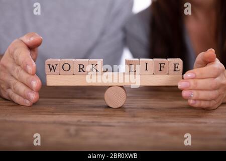Close-up Of Couple's Hand Protecting Work And Life Wooden Blocks Balancing On Seesaw Stock Photo