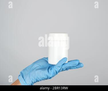 hand in blue sterile glove holds white plastic jar with pills on gray background, copy space Stock Photo