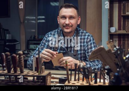 Man working with leather textile at a workshop. Male portrait. Concept of handmade craft production of leather goods. Stock Photo