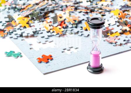 Pink and black sand hourglass on color puzzle pieces white background Stock Photo