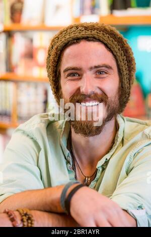 Smiling young man with knit cap in book store or library Stock Photo