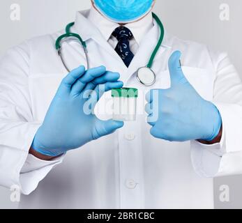 doctor in a white coat and blue sterile latex gloves holds a plastic jar for stool analysis, white background Stock Photo