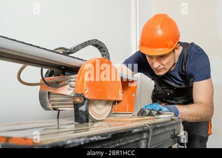 The worker is cutting a ceramic tile on a wet cutter saw  machine. Stock Photo