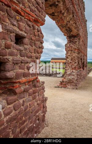 The remains of the Roman Basilica wall of the baths at Wroxeter with a view of a reconstructed Roman villa through the arch, Shropshire, England Stock Photo
