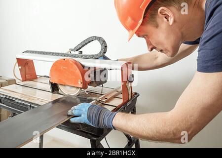 The worker is cutting a ceramic tile on a wet cutter saw  machine. Stock Photo