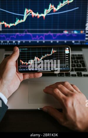 investment stockbroker stock market analysis. Financial investment app graph on phone and laptop. Multiple devices using.  hands close up. vertical ph Stock Photo