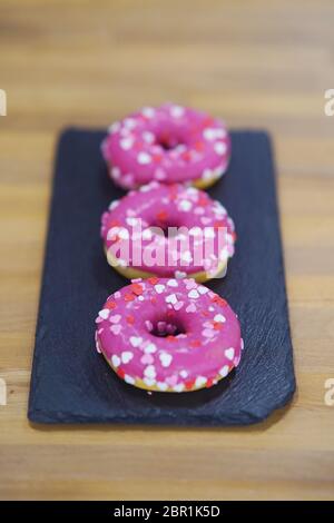 Three Pink donuts on a black tray. Stock Photo