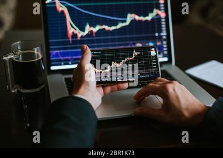 investment stockbroker stock market trading. Financial analysis using phone app and laptop. Market trading profit. Stock Photo