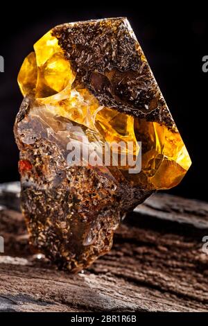 A piece of dirty amber with transparent yellow layer, has superficial cracks on its surface and many inclusions. Polished. Placed on piece of stoned w Stock Photo