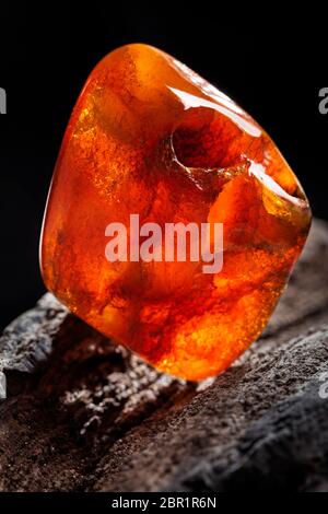 A piece of yellow semi transparent natural amber, classification color honey or cognac, has cracks on its surface. Polished, natural shape. Placed on Stock Photo