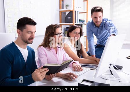 Young Businessman Explaining Plan To Colleagues On Compute At Workplace Stock Photo
