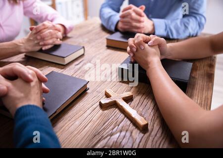 Close-up Of Businesspeople's Praying Hands Over The Bible On Wooden Desk Stock Photo