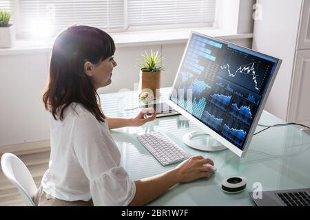 Young Female Stock Market Broker Analyzing Graph On Computer At Workplace Stock Photo