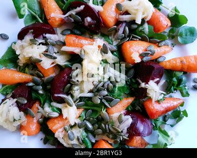 Carrot, beetroot and pupkin seed salad with baby spinach and rocket leaves on a white plate, cool light Stock Photo