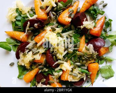 Carrot, beetroot and pupkin seed salad with baby spinach and rocket leaves on a white plate, warm light Stock Photo