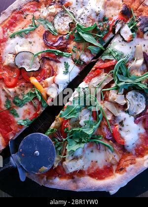 Cooked Mediterranian style wood fired pizza topped with fresh rocket, divided with a circular pizza cutter Stock Photo